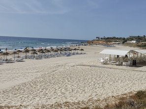 A beach with rows of sun loungers and umbrellas, a beachside restaurant, and a view of the ocean. - Magnificent south facing apartment, swimming pool, jacuzzi near sea and shops (Orihuela)