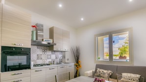 A modern kitchen with a built-in oven, a gas stove, and a sink. There is a dining area with a table and chairs, and a window with a view of the outdoors.