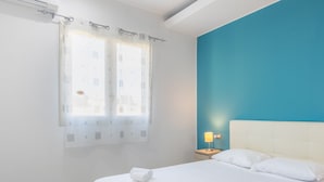 A bedroom with a bed, a nightstand, a lamp, and a window with curtains.