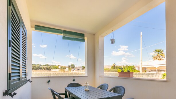 A balcony with a table and chairs, a hanging basket, and a view of the surrounding landscape. - Villa Demetra (Avola)