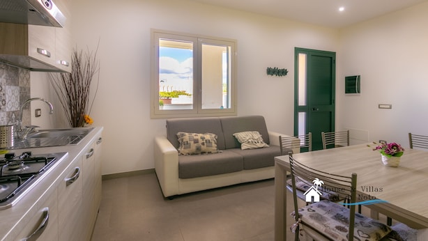 A modern kitchen with a built-in stove, a dining area with a wooden table and chairs, and a green door.