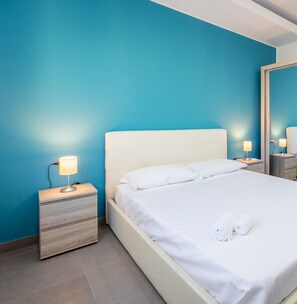Et hotelværelse med en seng, et natbord, en lampe og et spejl.
