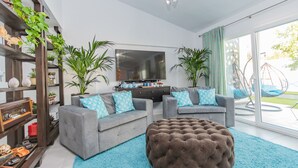 A modern living room with a grey sofa set, a large flat-screen TV, and a blue shag rug. There are potted plants and a wooden shelf with various items. - Cubo's Cozy & Modern Sol de Malaga / Private pool / Free Wifi (Málaga)