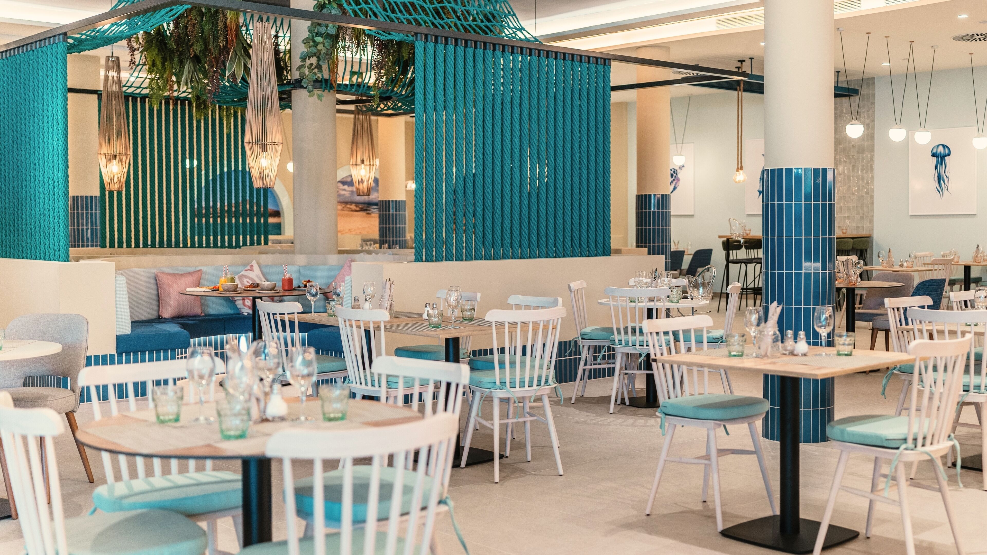 A modern restaurant with white and blue furniture, teal accents, and hanging lights.