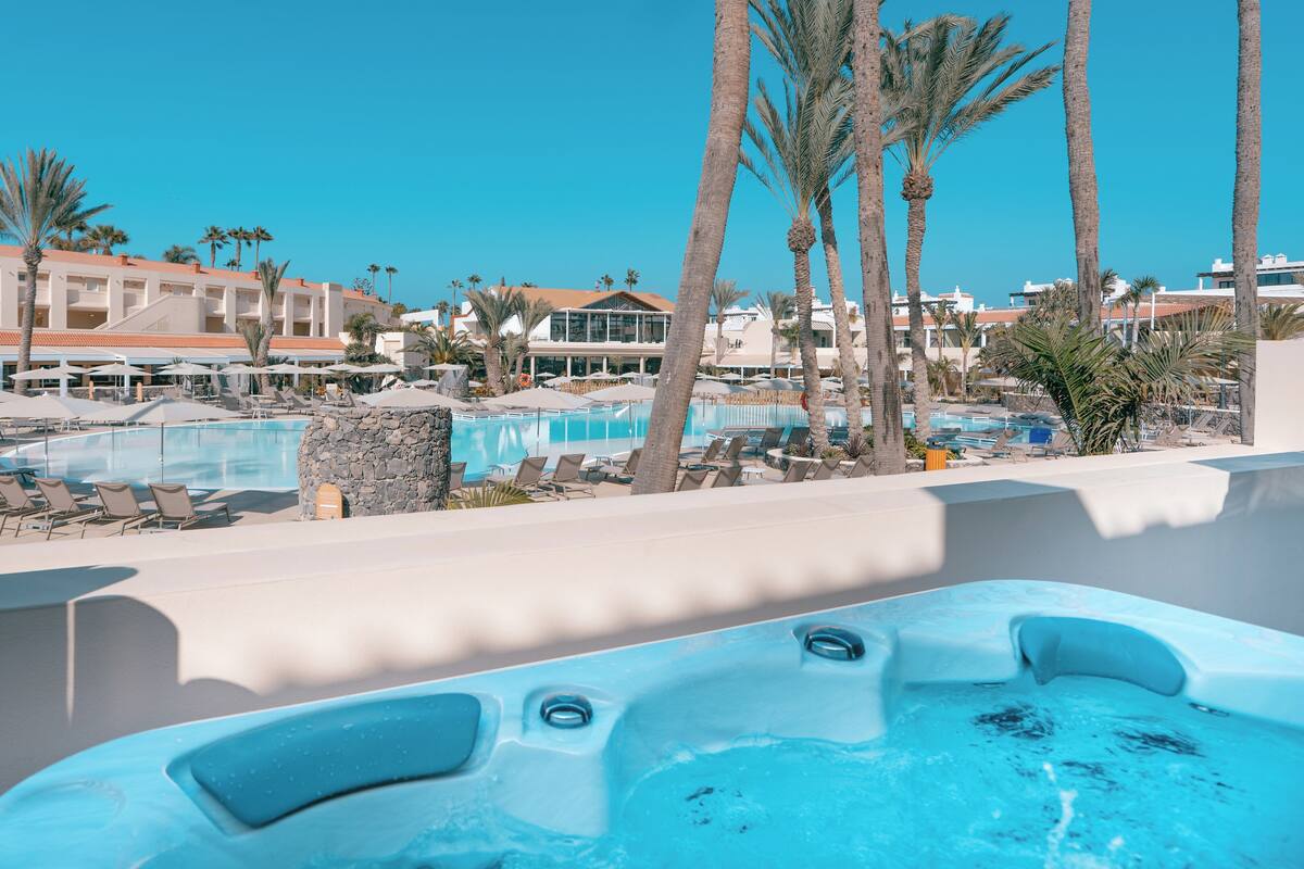 Uma área de piscina em resort, com várias piscinas, espreguiçadeiras e palmeiras.