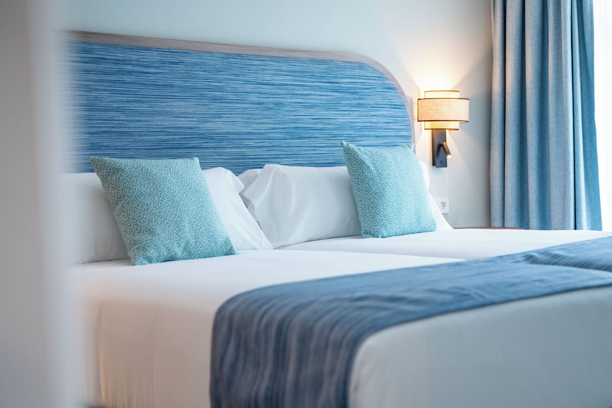 Uma cama bem arrumada com cabeceira azul, roupa de cama branca e almofadas azuis combinando.