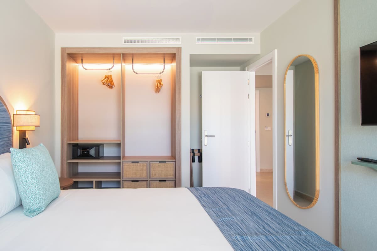 Quarto de hotel com uma cama, um guarda-roupa, um espelho e uma televisão.