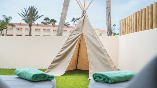 A teepee tent set up on artificial grass with a view of palm trees and a building in the background.