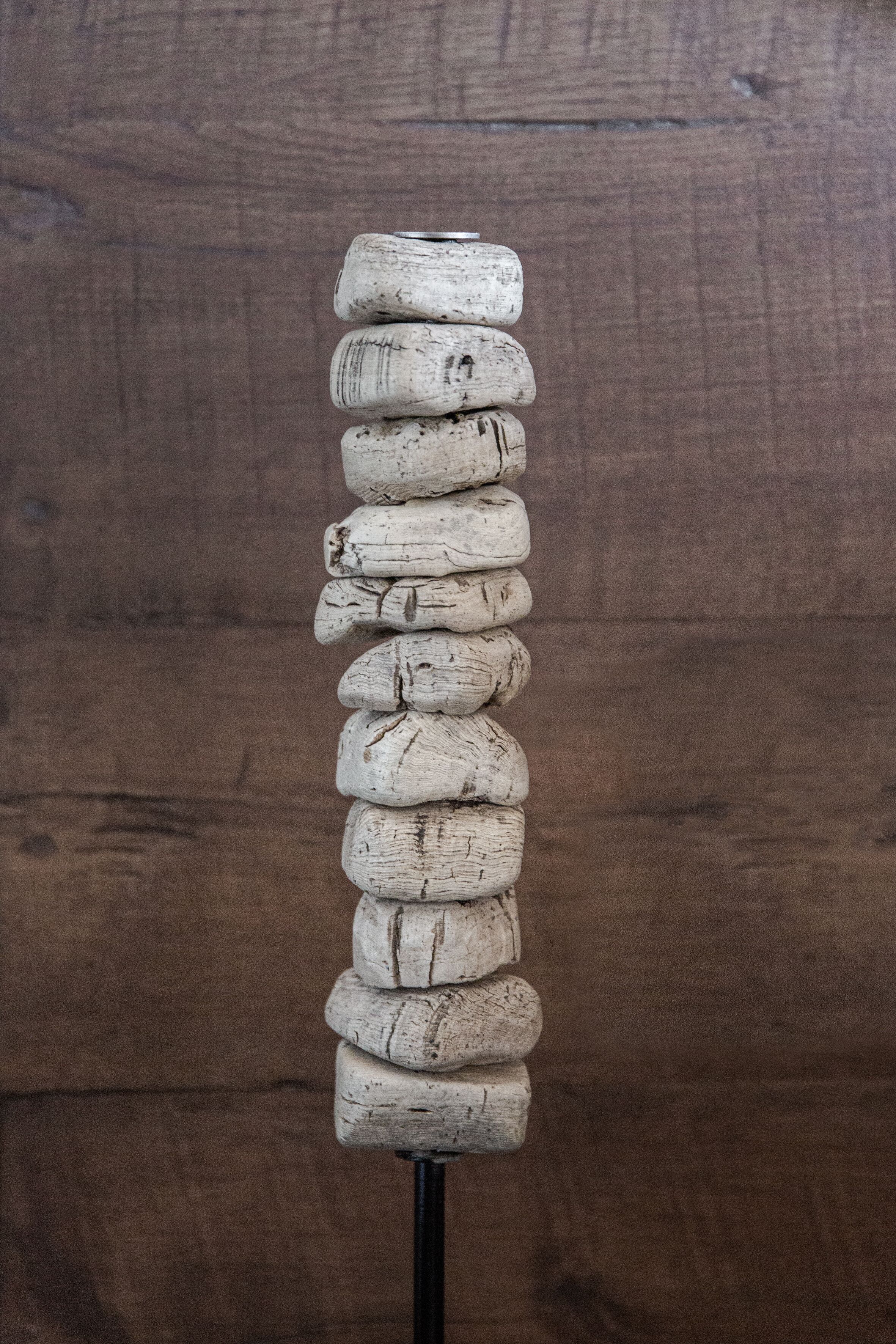 Una composición vertical de objetos cilíndricos, posiblemente botellas, apilados en una vara negra sobre un fondo de madera.