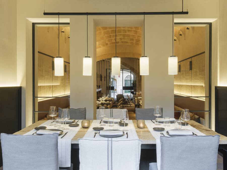 A modern dining area with a long table set for a meal, featuring pendant lighting and a view into the dining room.