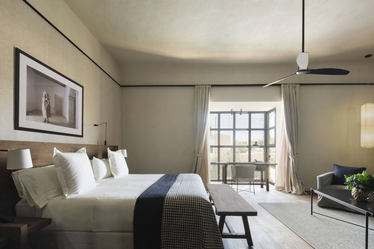 A hotel room with a large bed, a desk, a chair, a table, and a window with curtains.