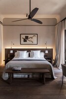 A hotel room with a large bed, a ceiling fan, a bedside table with a lamp, a framed picture on the wall, and a window with curtains.