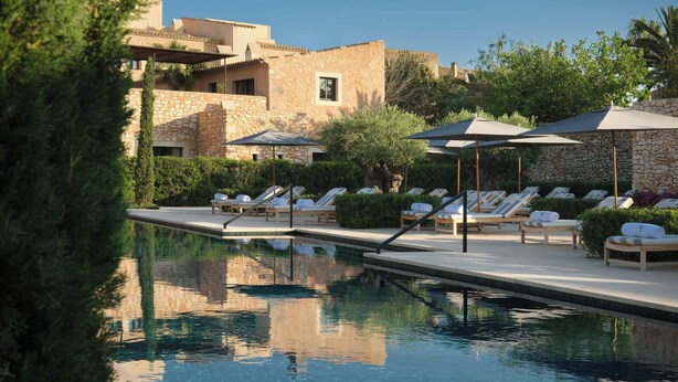 A pool area with lounge chairs and umbrellas, surrounded by stone buildings and greenery. - Can Ferrereta (Santanyi)