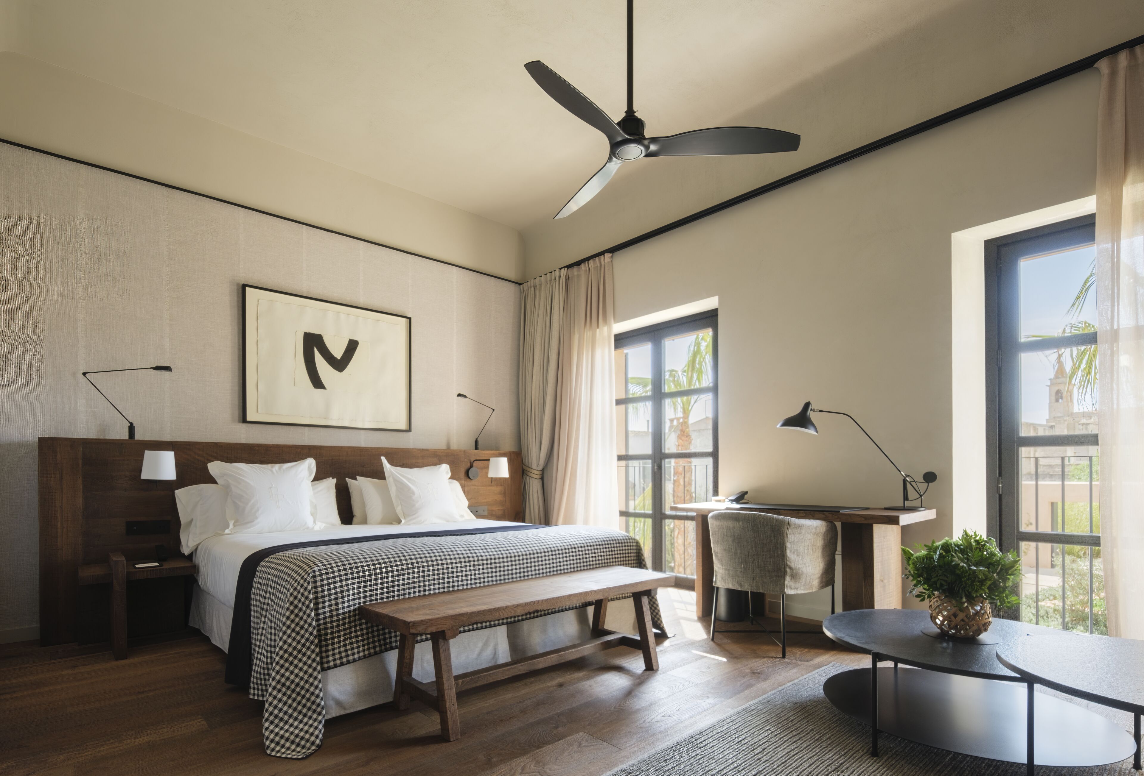 A modern hotel room with a large bed, a desk, a chair, and a ceiling fan.