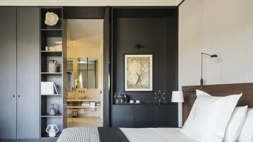 Une chambre moderne avec un grand lit, un mur foncé orné d’un tableau encadré, une table de chevet avec une lampe et une armoire intégrée.