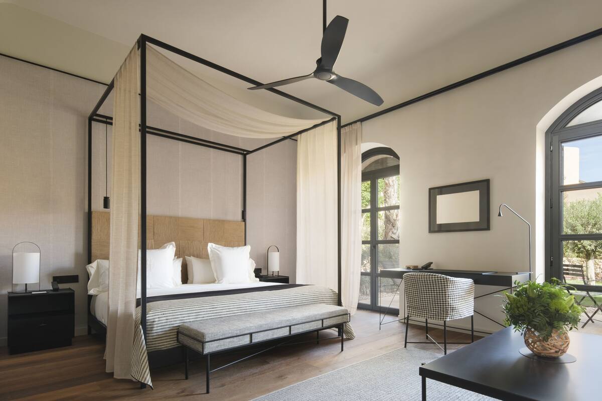 A four-poster bed with a canopy, a desk with a chair, and a potted plant.