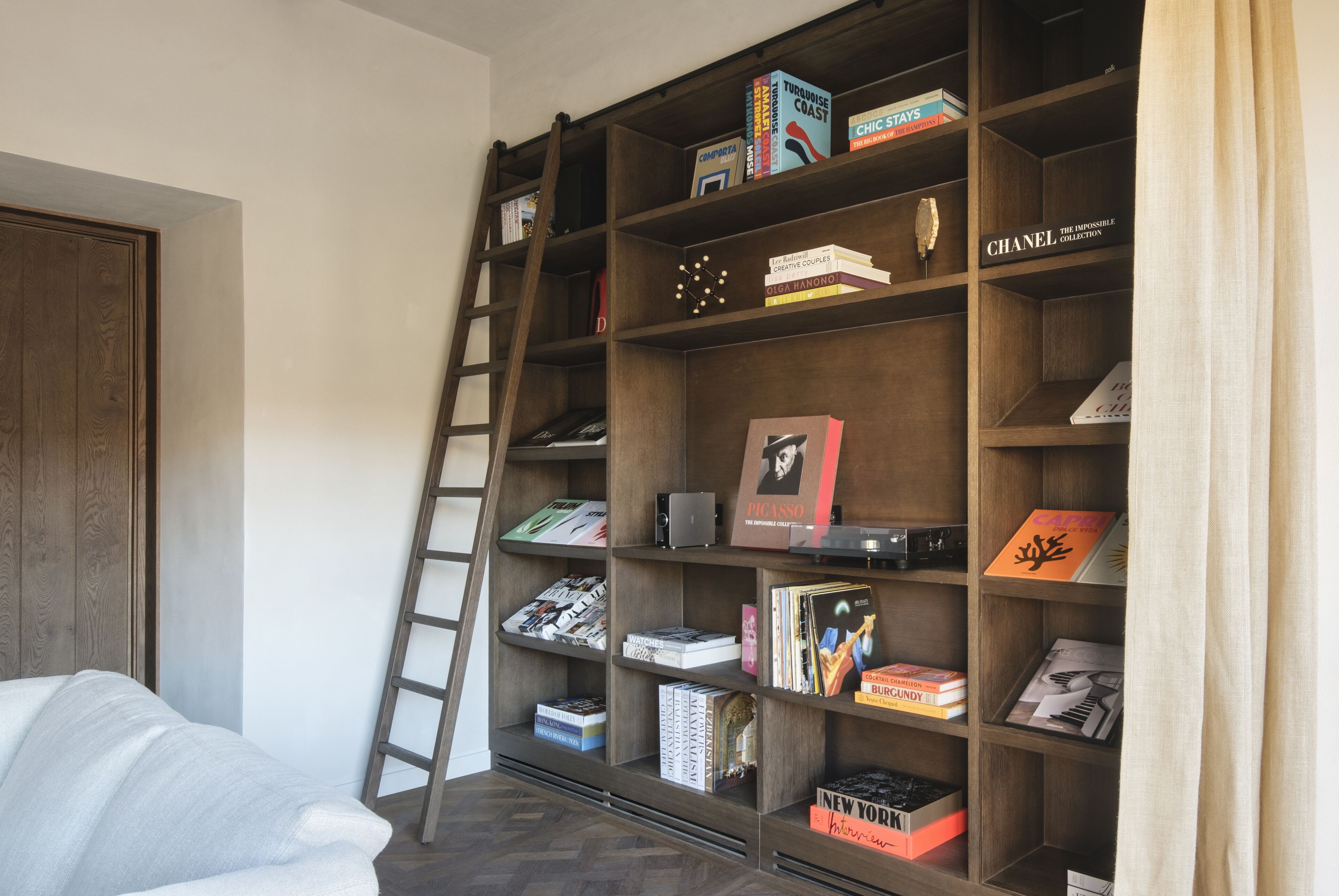 Ein Bücherregal mit Büchern und Dekorationselementen, eine Leiter und ein weißes Sofa.