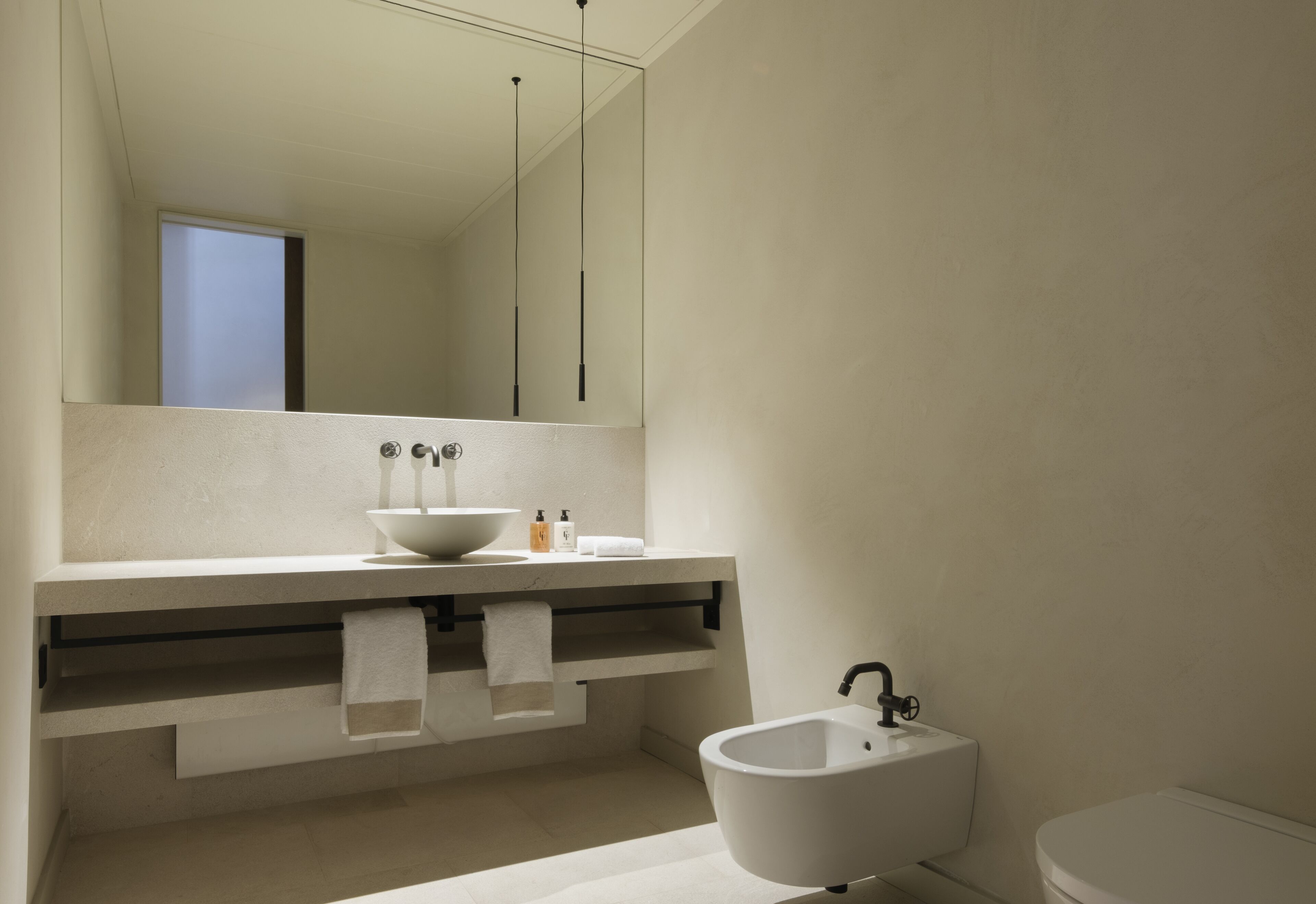 A modern bathroom with a large mirror, a sink, a bidet, and a toilet.