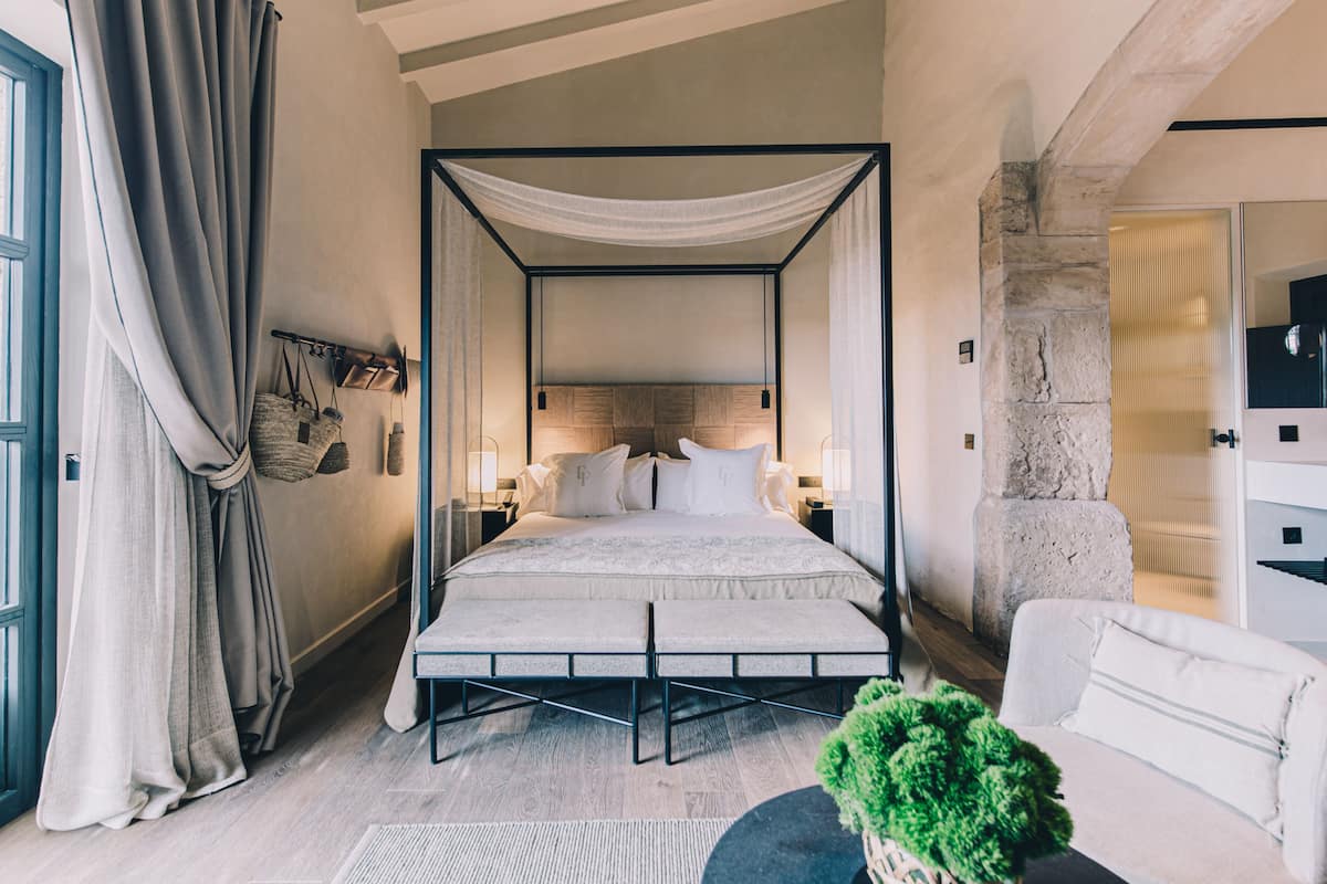 A four-poster bed with a canopy, a white sofa, a green plant, and a stone wall.