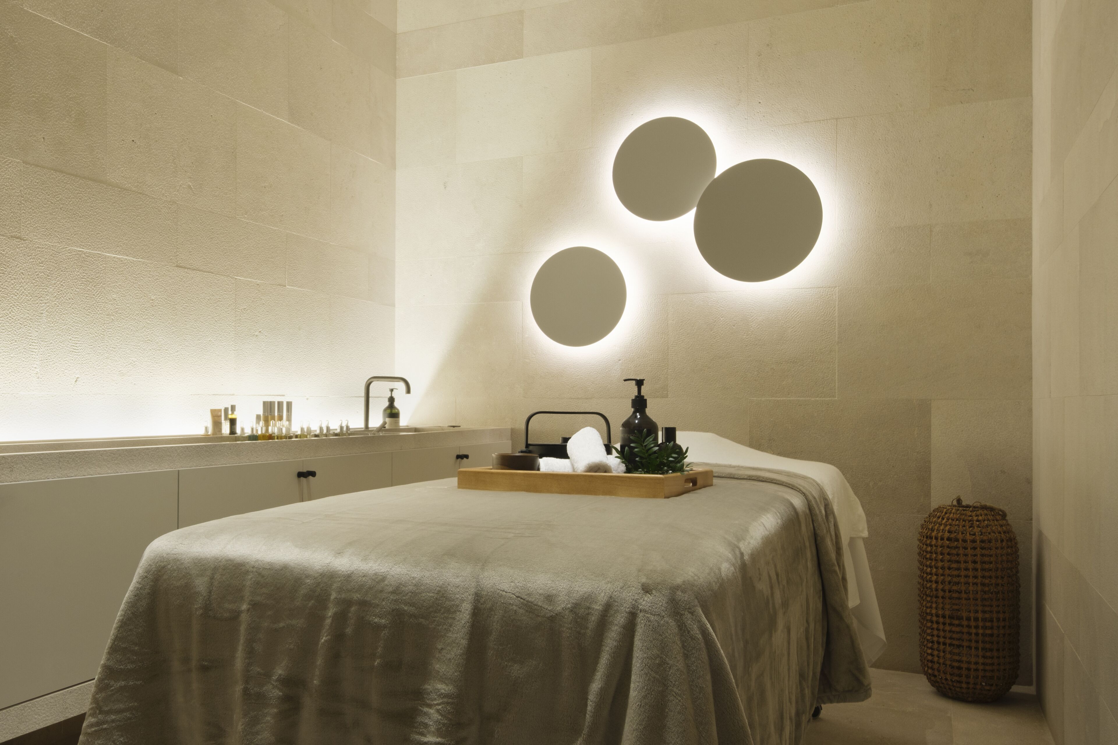 Een moderne badkamer met een groot bed, een dienblad met toiletartikelen en een rond wandarmatuur.