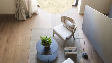 A room with a large window, a round table with a plant, two wicker chairs, and a hanging light fixture.