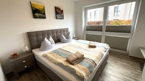 Une chambre moderne avec un grand lit, deux oreillers, une table de chevet avec une lampe et une fenêtre avec des stores.