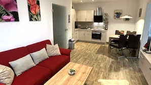 Un salon moderne avec un canapé rouge, une table basse en bois et une cuisine en arrière-plan.