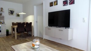 Un salon moderne doté d’un téléviseur à écran plat, d’un coin repas avec une table et des chaises, et d’un vase décoratif posé sur une table basse.