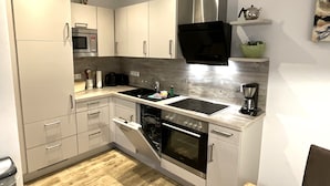 Une cuisine moderne avec des armoires blanches, une hotte de cuisinière en acier inoxydable, un four encastré et un four à micro-ondes.