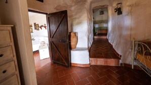 A narrow hallway with a rustic, white-walled interior, a wooden door, a large ceramic pot, and a bed with a green bedspread in the background. - Villa Paiare with private pool on the Ionian sea (Torre Vado)