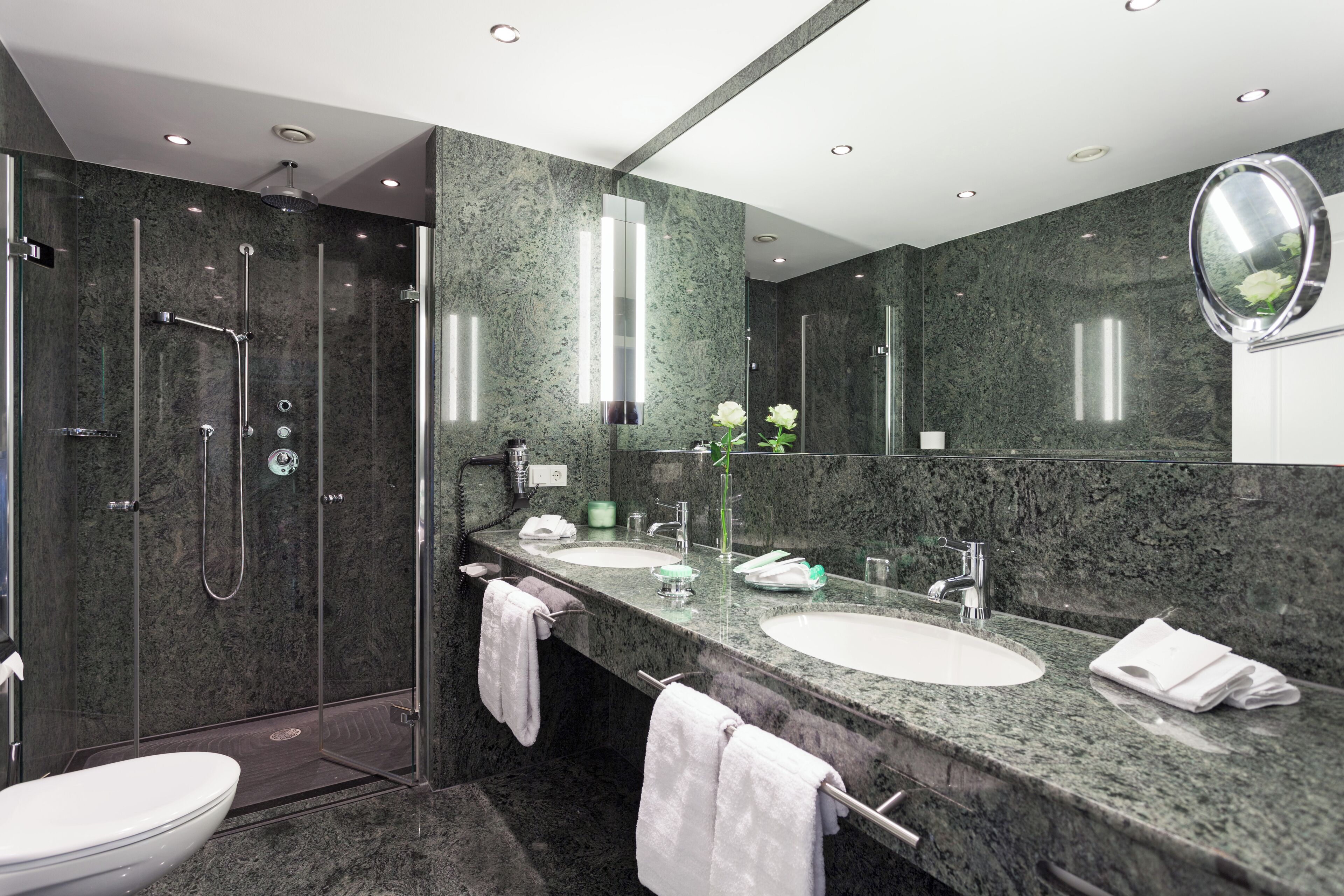 Een moderne badkamer met een douche in een glazen cabine, twee wastafels en een grote spiegel.