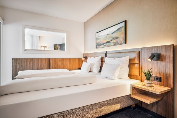 Een moderne hotelkamer met een groot bed, een nachtkastje met lamp, een spiegel en een schilderij aan de muur.