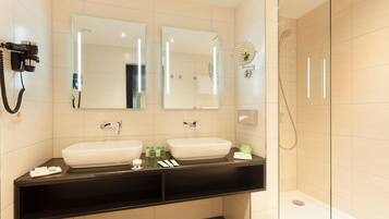 A modern bathroom with two sinks, a hairdryer, and a glass-enclosed shower.