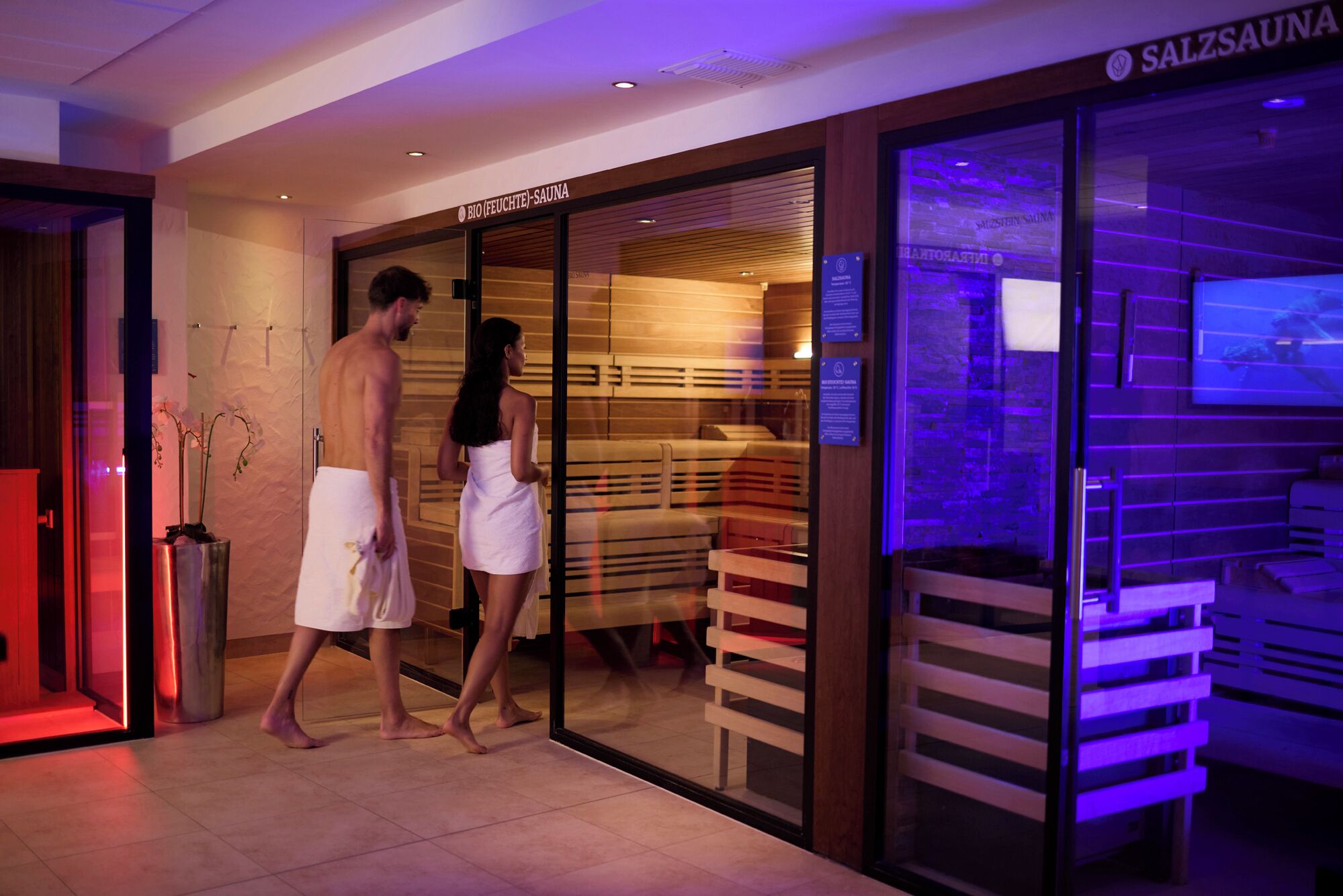 Der Eingang eines Spas mit Glastür, Holzbanken im Inneren und einem Schild mit der Aufschrift 'BIO (FEUCHTE) SAUNA'.