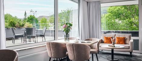 Ein modernes Wohnzimmer mit Essbereich, großen Fenstern und einem Balkon mit Gartenmöbeln.