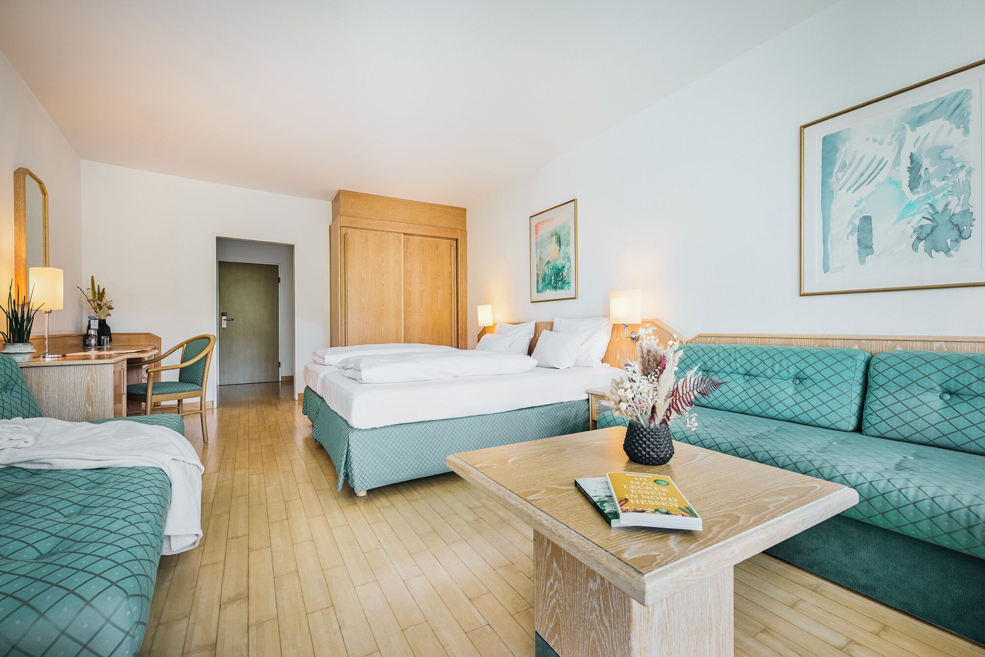 Een hotelkamer met een bed, een bank, een salontafel, een bureau met lamp en een deur.