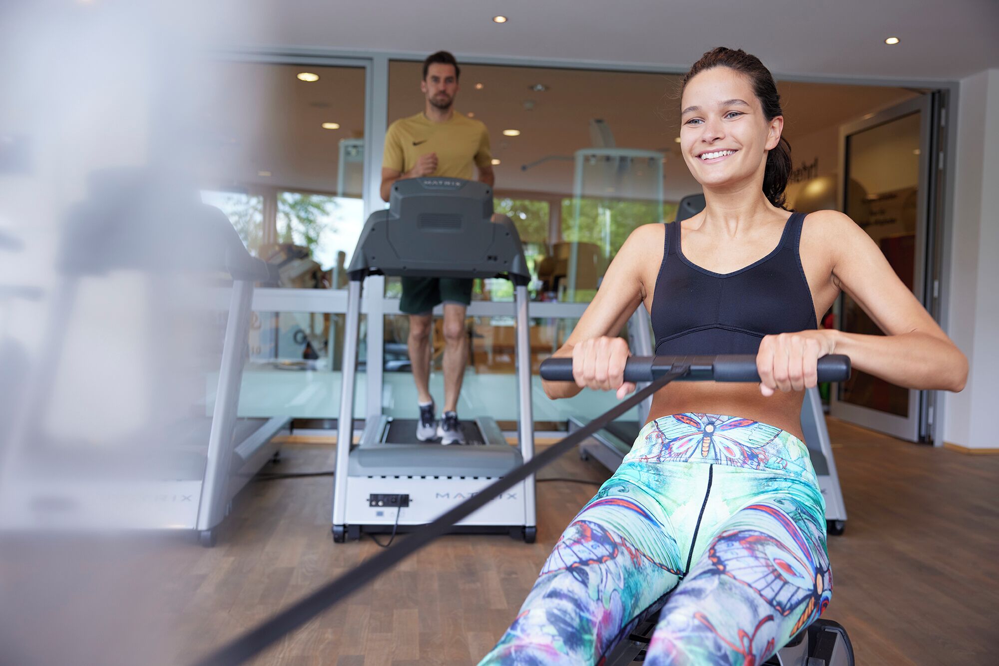 A gym with cardio machines, a treadmill, and a person using a rowing machine.