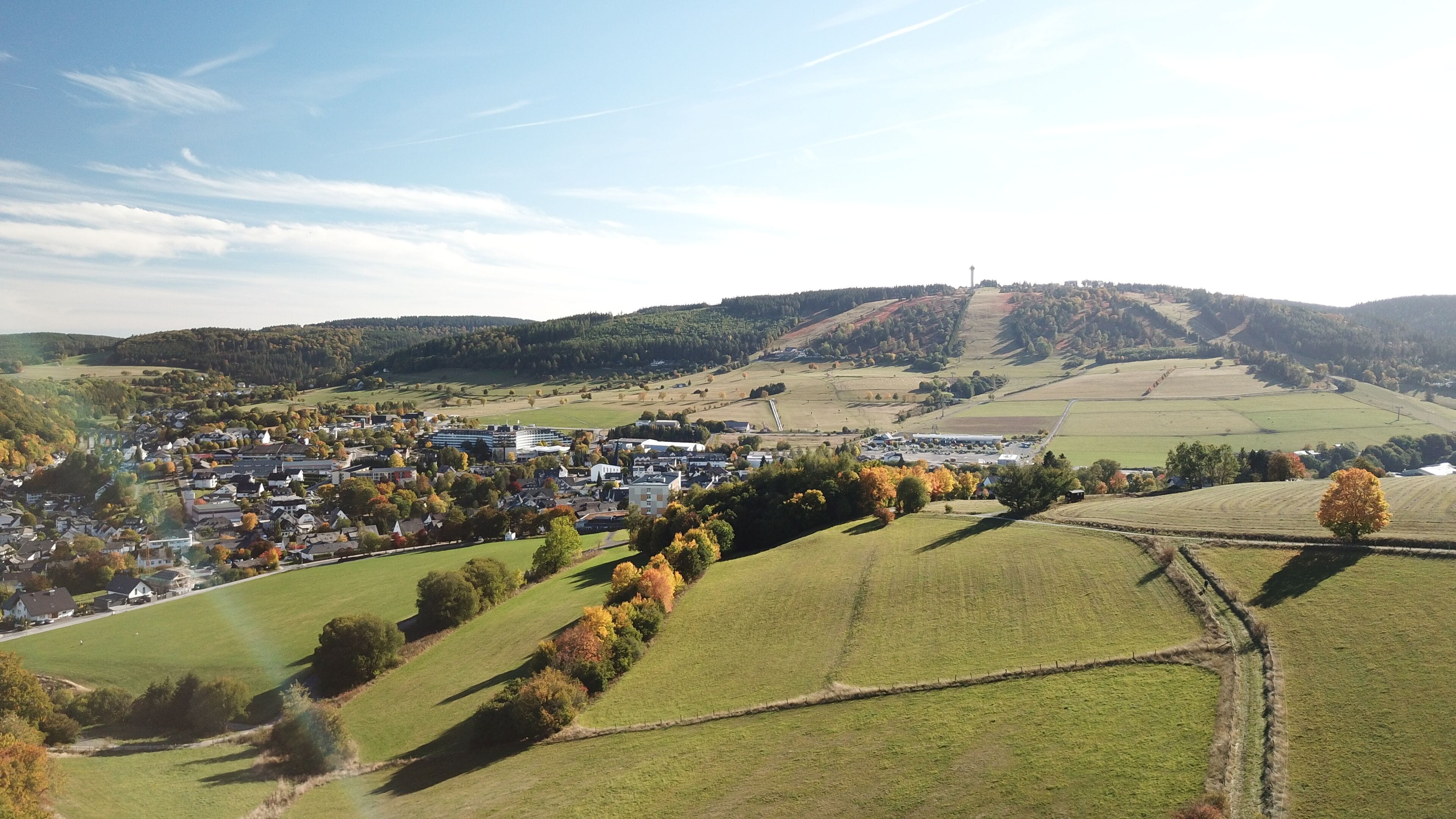 A rural town with a mix of residential and commercial buildings, surrounded by rolling hills and fields.