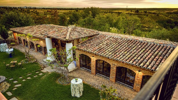 A villa with a tiled roof, brick walls, and a well-maintained garden with a lawn and stone pathway.