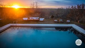A swimming pool with lounge chairs and a view of the sunset.