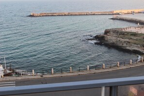 A coastal view with a rocky shoreline, a pier extending into the water, and a paved walkway along the edge.