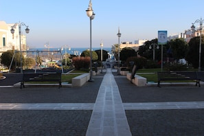 A paved walkway with benches, street lamps, and a clear view of the sea in the distance.
