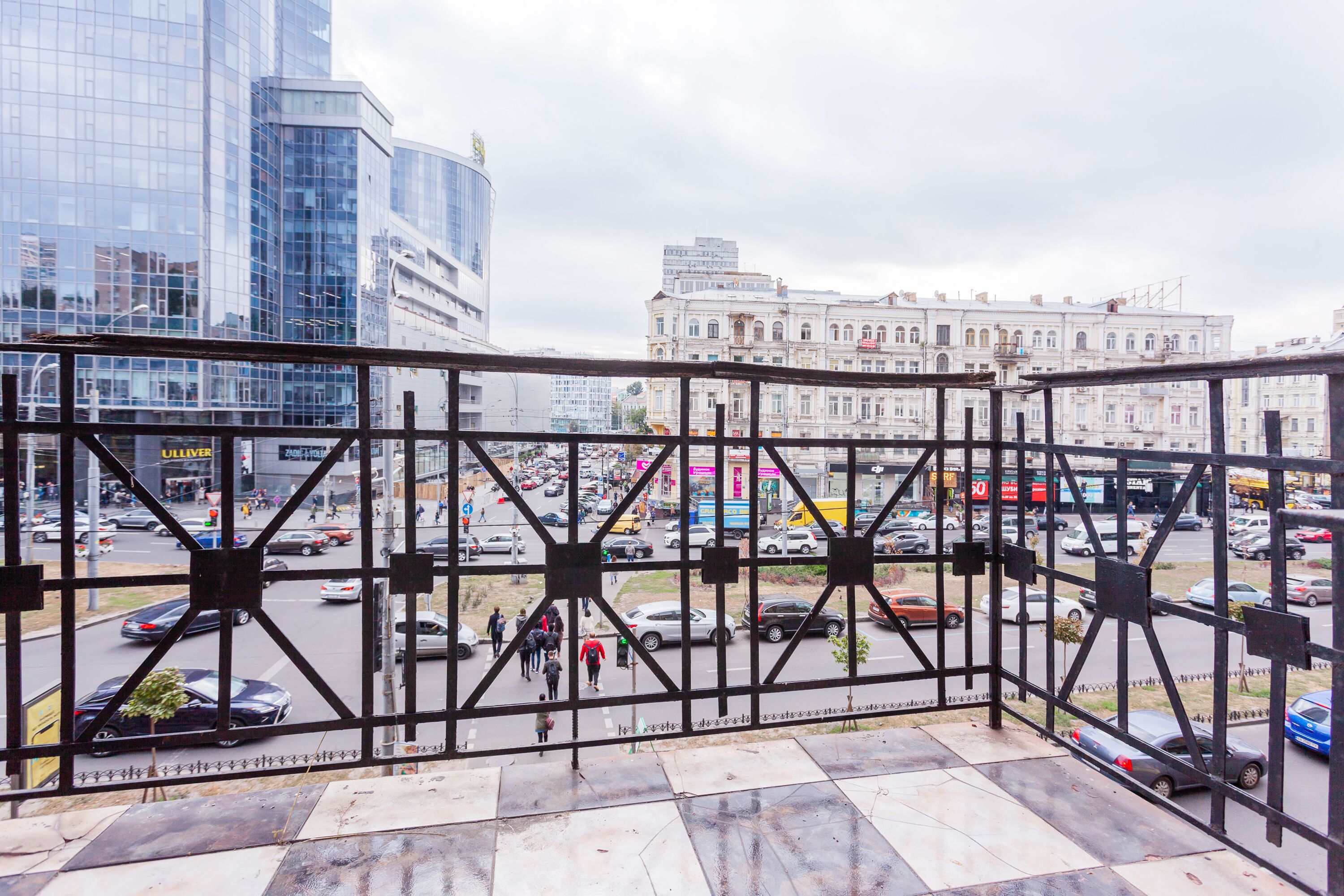 A view from a balcony overlooking a busy street with modern and historic buildings.