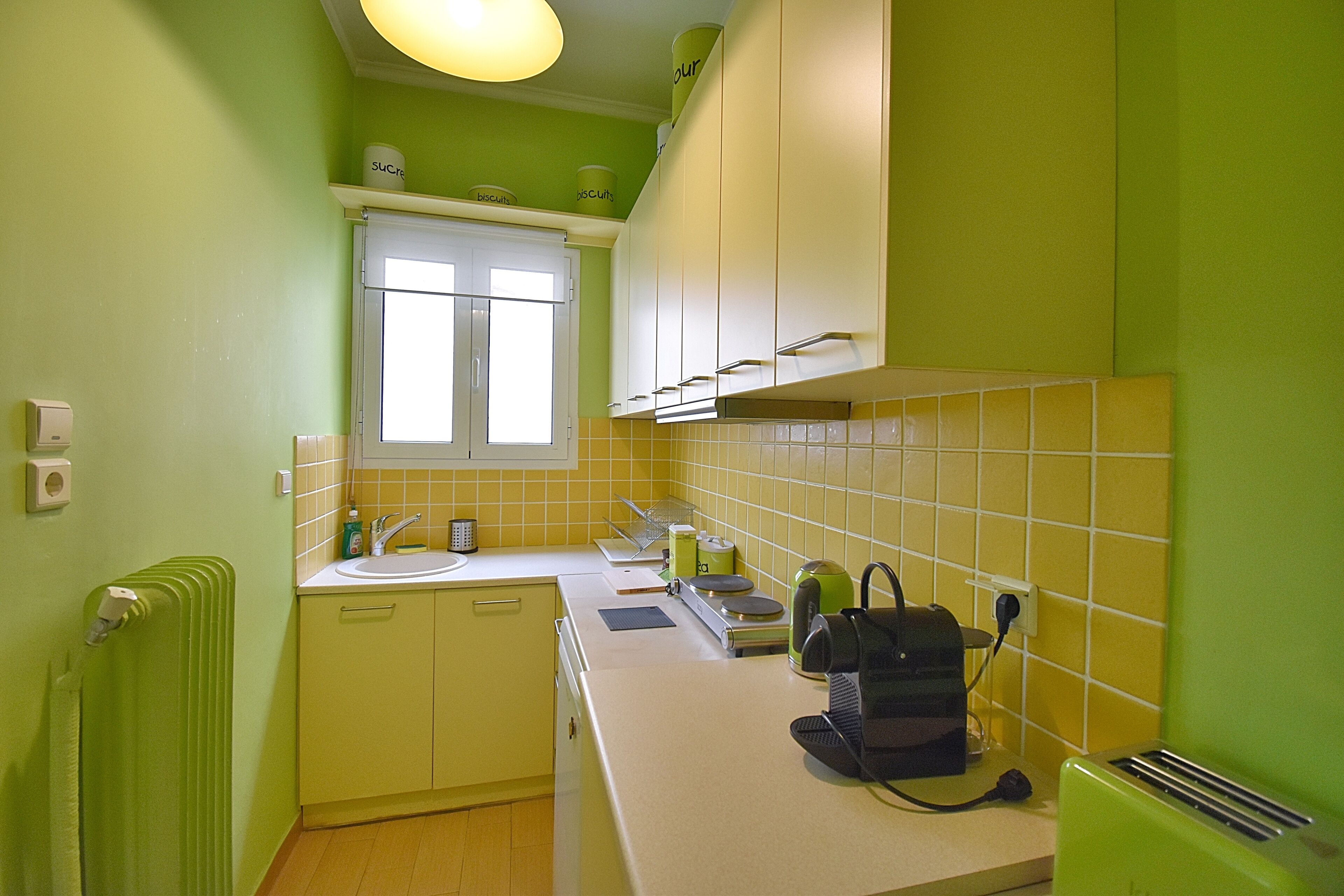 Une cuisine avec des murs verts, une fenêtre, un évier et un grille-pain.