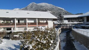 Un edificio cubierto de nieve con un balcón, un pequeño puente y una montaña al fondo.