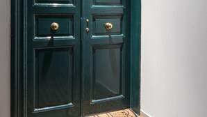 A dark green double door with a brass doorknob and a brass handle, leading to a tiled entrance area. - MAISON SALONIQUE 1930 (Thessaloniki)