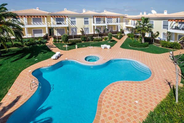 Une piscine dotée d’une terrasse carrelée, entourée d’une pelouse bien entretenue et de palmiers.