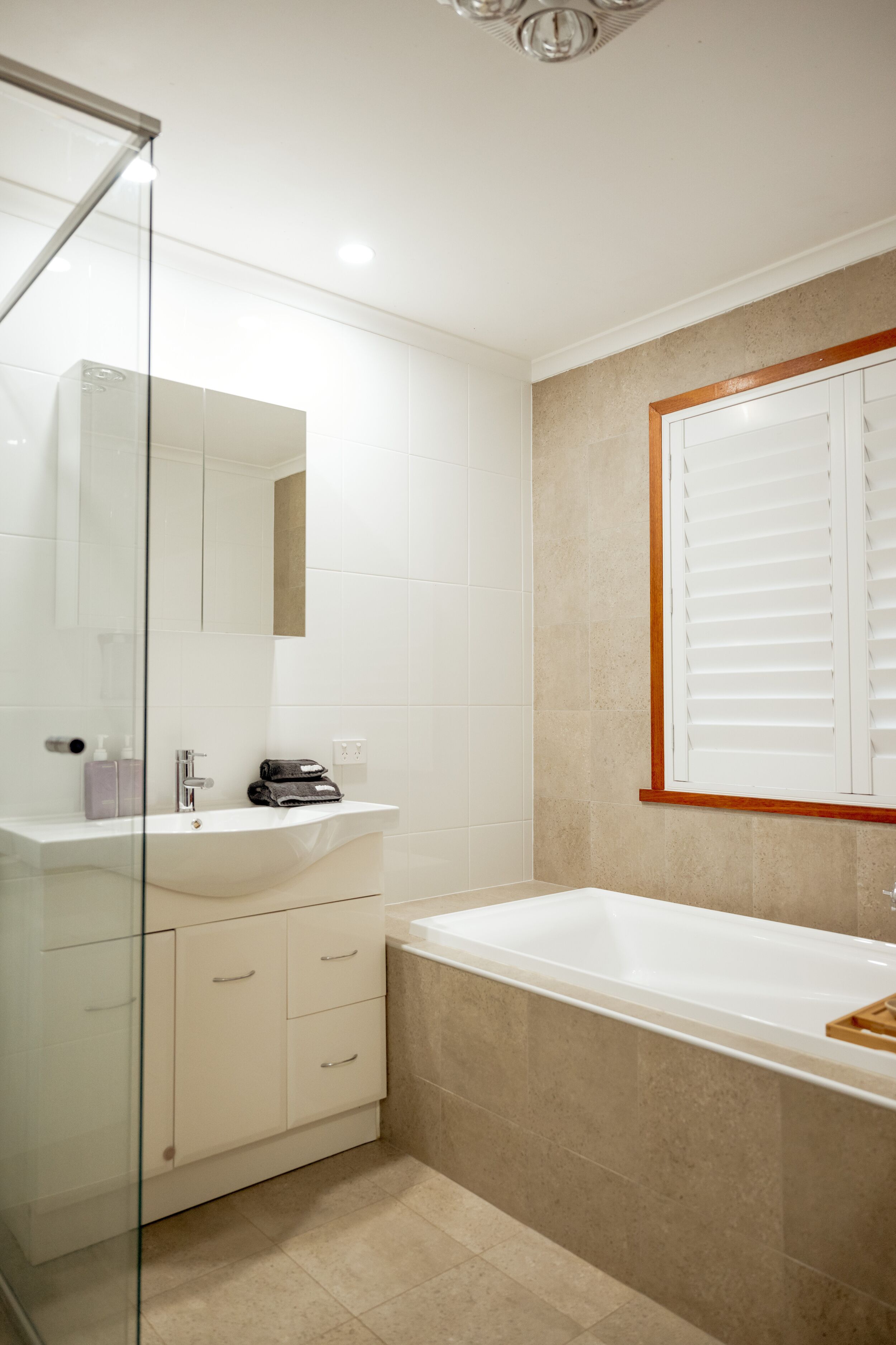 A modern bathroom with a glass shower enclosure, a white sink with a mirror, and a bathtub.