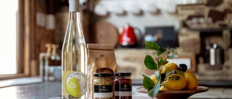 A kitchen counter with a wine bottle, jars of preserves, and a bowl of citrus fruits.