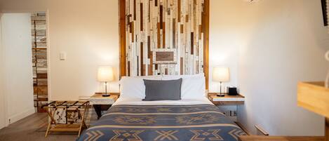A neatly arranged bedroom with a bed, two bedside tables, a wall-mounted air conditioner, and a wooden headboard with a decorative panel.